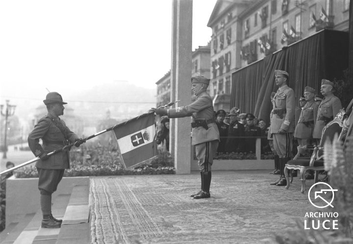 Vittorio Emanuele, su un palco allestito in piazza Vittorio a Torino, consegna una ricompensa al valore alla bandiera di un reggimento della Divisione Tridentina, 1942