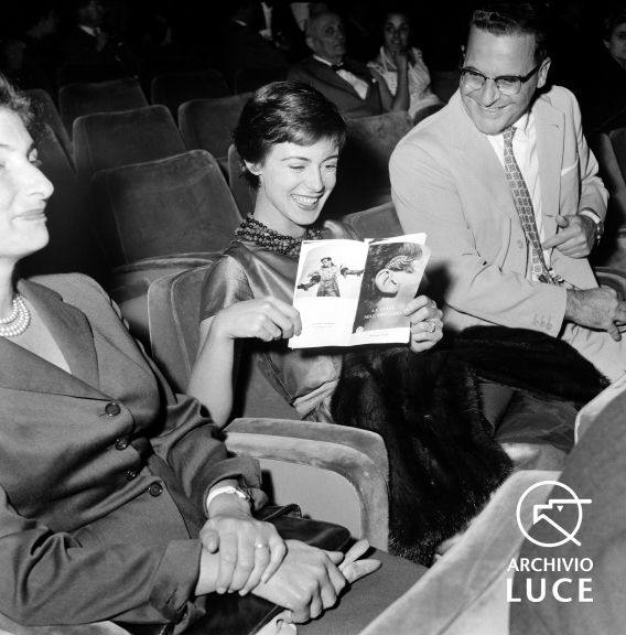 Anna Maria Ferrero seduta in platea ride sfogliando un dépliant dedicato a uno spettacolo teatrale, 1957